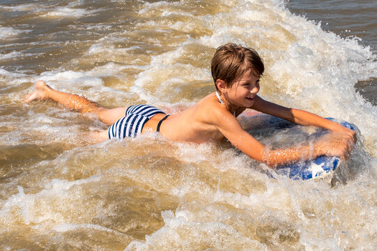 Young beach boy on a boogie board swimming in the ocean waves