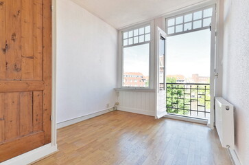 an empty room with wood flooring and sliding door leading out to the balcony overlooking cityscar...