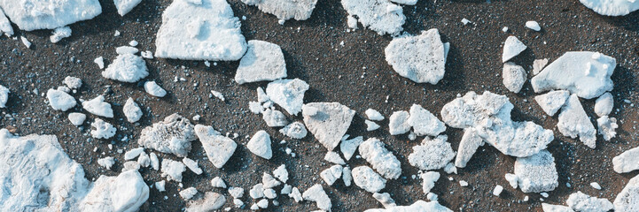Top view of the ice floes on the shore. Melting ice on a pebble sea beach. White ice floes on a dark background. Climate change in the Arctic. Wide panorama.
