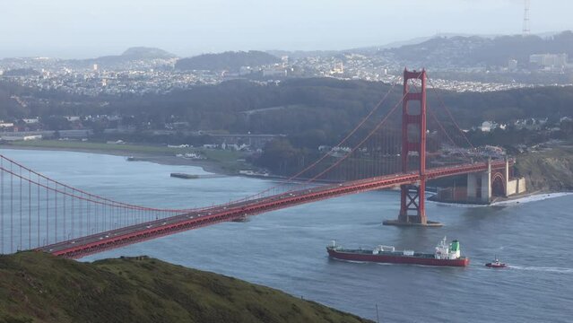 Cargo ship with tug sails under Golden Gate Bridge to port in San Francisco Bay