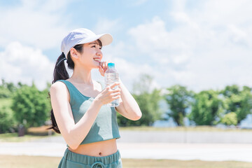 公園で水・ミネラルウォーターを飲む女性（水分補給・運動・ワークアウト・ランニング・ウォーキング）
