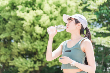 公園で水・ミネラルウォーターを飲む女性（水分補給・運動・ワークアウト・ランニング・ウォーキング）
