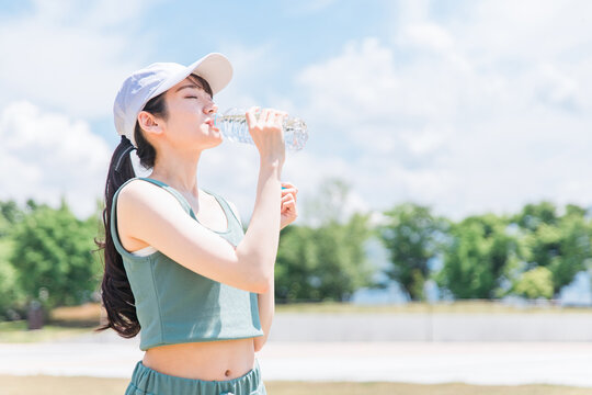 公園で水・ミネラルウォーターを飲む女性（水分補給・運動・ワークアウト・ランニング・ウォーキング）

