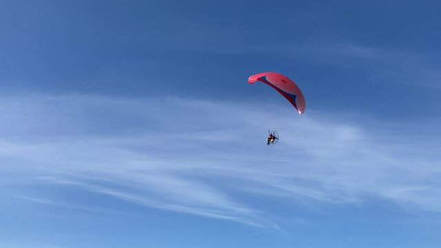 Complete panorama with a red and blue paraglider low in the sky captured by a fast left-panning camera and reaching to the distant sunny horizon amongst soft, smooth and silky clouds in the azure