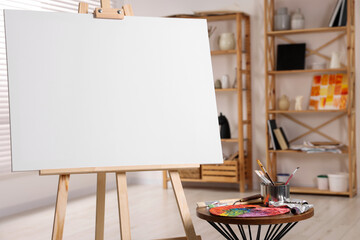Wooden easel with blank canvas and different art supplies in studio, closeup