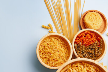 Bowls with different types of raw pasta on light background, closeup