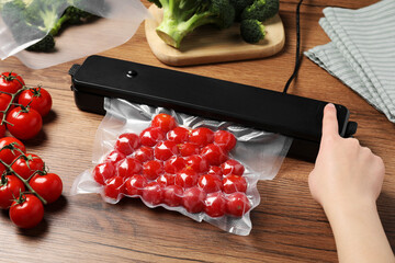 Woman packing cherry tomatoes using vacuum sealer on wooden table, closeup