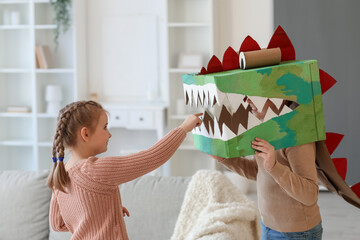 Little girl playing with her brother in cardboard dinosaur costume at home