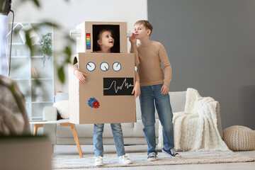 Little girl in cardboard robot costume playing with her brother at home