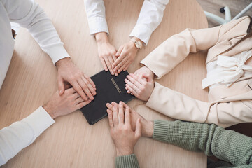 Group of business people praying with Holy Bible at table in office, top view