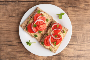 Fresh crunchy crispbreads with pate, tomatoes, red onion and greens on wooden table, top view