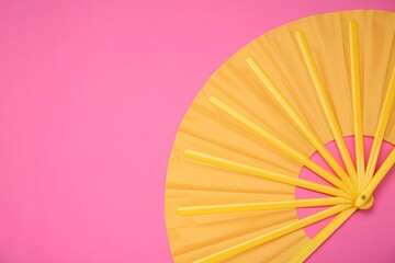 Bright yellow hand fan on pink background, top view. Space for text