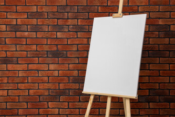 Wooden easel with blank canvas near brick wall. Space for text