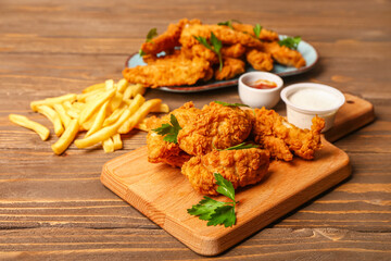Board with tasty nuggets, sauces and french fries on wooden background