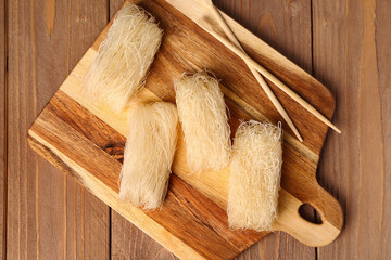 Cutting board with raw rice noodles and chopsticks on wooden board