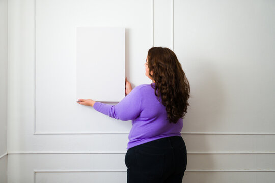 Rear view of a fat woman putting up a picture decoration