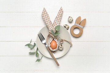 Table setting with fork and egg in napkin on white wooden background
