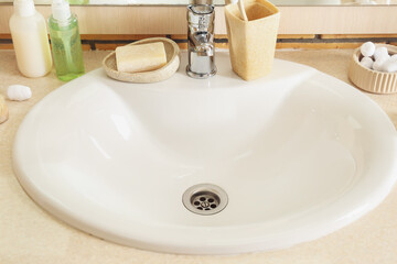 Table with white ceramic sink and bath supplies in room, closeup