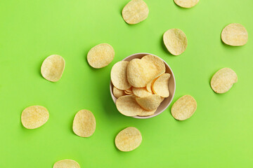 Bowl with delicious potato chips on green background