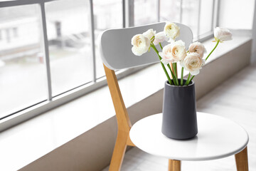 Vase with ranunculus flowers on chair near window in room, closeup