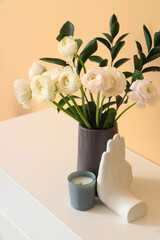 Vase with ranunculus flowers and decor on chest of drawers near beige wall