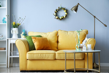 Interior of living room with yellow sofa and Easter wreath on light wall