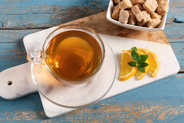 Board with cup of tasty green tea, lemon slices and cane sugar on color wooden background