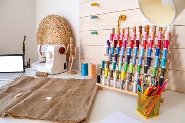 Tailor's workplace with thread spools, sewing machine and laptop in atelier