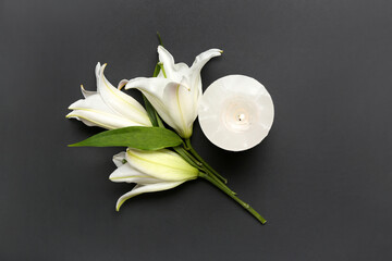 Burning candle and white lily flowers on dark background