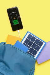 Bag with notebooks and portable solar panel charging mobile phone on yellow background
