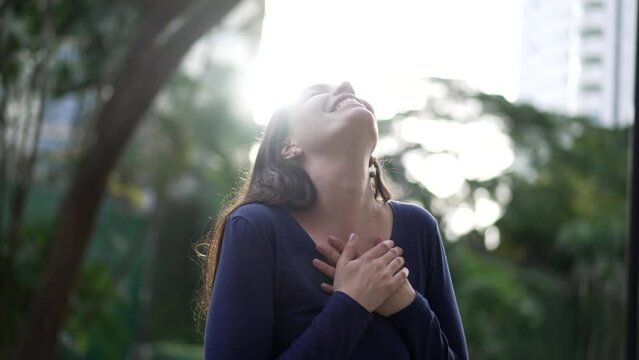 Grateful woman standing outside hands in chest feeling HAPPINESS and FREEDOM