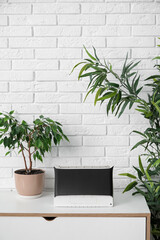 Air purifier and houseplants on chest of drawers near white brick wall