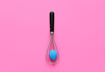 Whisk with Easter egg on pink background