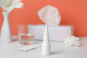 Fototapeta na wymiar Nasal drops with pills, glass of water and tissues on table near red wall. Seasonal allergy concept