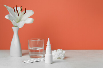 Nasal drops with pills, flower, glass of water and tissue on table near red wall. Seasonal allergy concept
