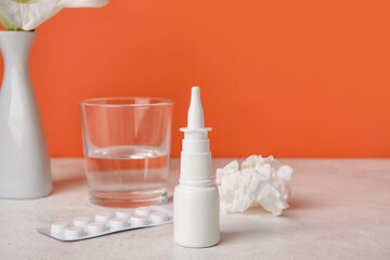 Fototapeta na wymiar Nasal drops with pills, glass of water and tissue on table near red wall. Seasonal allergy concept