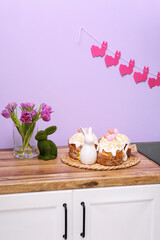 Easter cakes, bunnies and vase with tulip flowers on kitchen counter near lilac wall