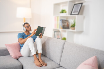 Young man, seriously turning the pages of an old book while wearing his headphones, sitting in the living room