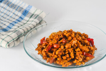 sliced tempeh fried dry with chilies and peanuts or orek tempe served on a small plate with a napkin isolated on a white background