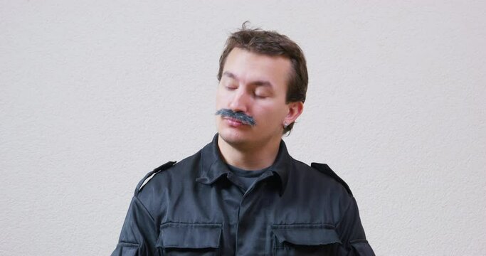 Suspicious man with mustache looks to sides shaking head. Young security guard in black jacket shows curiosity standing against white wall closeup