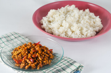 sliced tempeh fried dry with chilies and peanuts or orek tempe served on a small plate  and a plate of white rice isolated on a white background