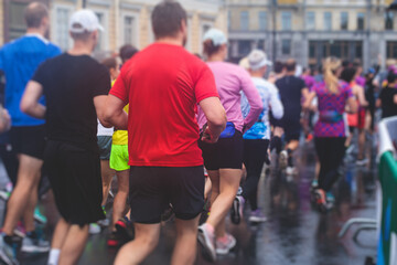 Marathon runners crowd, participants start running the half-marathon in the city streets, crowd of joggers in motion, group athletes outdoor training competition in the rain