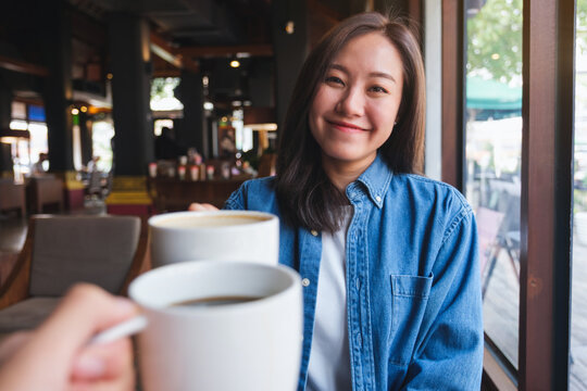 Portrait image of a young woman clinking coffee cups with friends in cafe