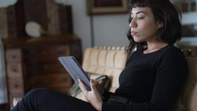 One hispanic young woman using tablet browsing internet online sitting at elegant living room