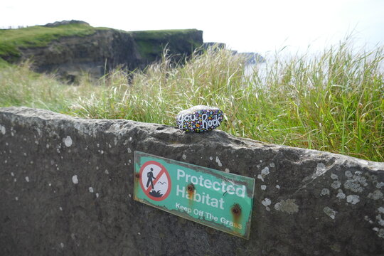 Protected habitat sign on old stone wall with kindness rock on top	
