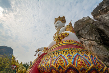 The white Buddha statue with rock mountain in the background at Tham Champathong monastery, Ratchaburi, Thailand