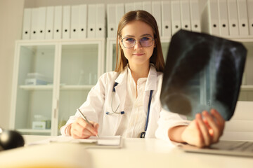 Young doctor in glasses holds chest x-ray and looks at camera.