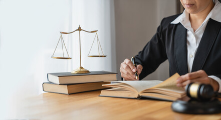 Asian female lawyer or legal advisor working on the scale of justice sitting at her desk and holding a pen to look at the information Detailed content about the scale of jurisprudence to study.