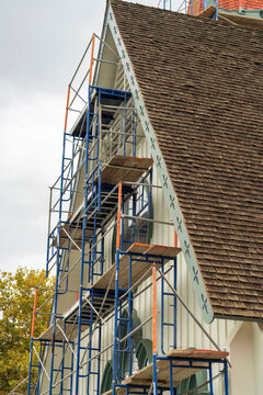 Scafolding Above Side Of Building For Construction Projects And Workers With Brown Roof Tiles On A Frame Style Building