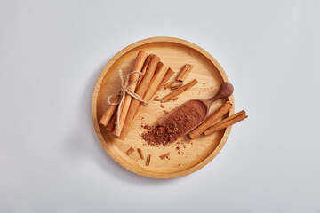 Top view, flat lay with cinnamon sticks and powder on wooden dish, isolated on light background. Medicinal herbs, cooking spices, cosmetic flavorings